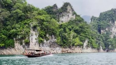 Geleneksel bir tekne Khao Sok Ulusal Parkı 'nın kristal berrak sularında süzülüyor, yemyeşil ve yüksek kireçtaşı kayalıklarıyla çevrili. Bu sakin manzara bölgenin doğal güzelliğini ve biyolojik çeşitliliğini gözler önüne seriyor..