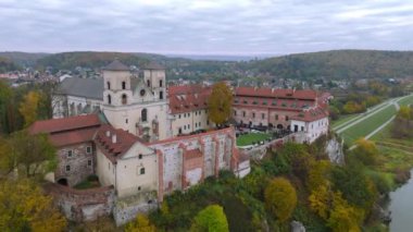 Yeşillik ve canlı sonbahar renkleriyle çevrili tarihi bir Benedictinemonastery 'nin çarpıcı bir görüntüsü. Mimari, kayan tepeler ve uzaktaki antika evlere karşı kurulmuş zengin bir mirası yansıtıyor. Tyniec, Polonya.