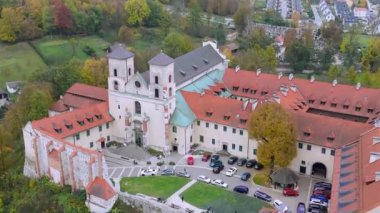 Yeşillik ve canlı sonbahar renkleriyle çevrili tarihi bir Benedictinemonastery 'nin çarpıcı bir görüntüsü. Mimari, kayan tepeler ve uzaktaki antika evlere karşı kurulmuş zengin bir mirası yansıtıyor. Tyniec, Polonya.