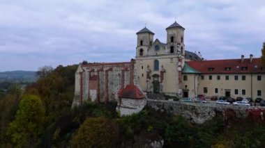 Yeşillik ve canlı sonbahar renkleriyle çevrili tarihi bir Benedictinemonastery 'nin çarpıcı bir görüntüsü. Mimari, kayan tepeler ve uzaktaki antika evlere karşı kurulmuş zengin bir mirası yansıtıyor. Tyniec, Polonya.