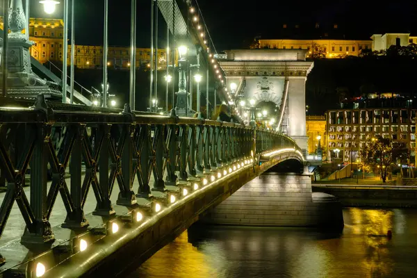 Zincir Köprüsü, Tuna Nehri üzerinde geceleri sokak lambalarıyla aydınlatılan görkemli bir şekilde duruyor. Bu ikonik simge Buda ve Pest 'i birbirine bağlıyor. Nehir kıyısı boyunca çarpıcı bir mimari ve canlı şehir hayatı sergiliyor..