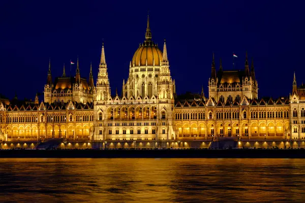 Macar Parlamento Binası, karmaşık mimarisini ve Tuna Nehri 'nin sularına yansımasını gösteren, gece gökyüzüne karşı güzelce aydınlatılmış duruyor. Macaristan, Budapeşte 'de çarpıcı bir manzara.