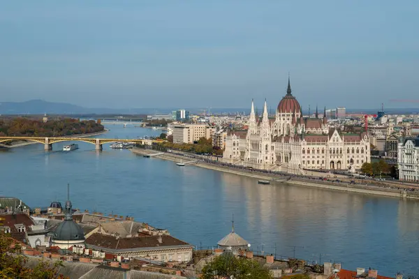 Budapeşte 'deki Tuna Nehri boyunca uzanan ikonik Macar Parlamento Binası' nın çarpıcı bir manzarası. Açık mavi gökyüzü, mimari güzelliği ve hayat dolu şehir yaşamını gözler önüne seren resim sahnesini tamamlıyor..