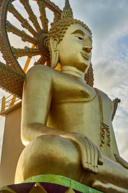 Görkemli bir altın Buda heykeli manzaralı bir arka planda huzur içinde duruyor. Wat Phra Yai olarak bilinen bu ikonik anıt, Koh Samui, Tayland 'da barışı ve maneviyatı temsil eden popüler bir cazibedir..