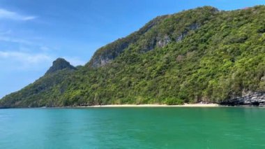 Bu çarpıcı manzara, altında el değmemiş bir plaj bulunan sakin bir turkuaz denizin üzerinde yükselen canlı yeşil bir yamacı gösteriyor. Tayland 'da ünlü bir tropik cennet olan Ang Thong Ulusal Parkı' nın güzelliğini yansıtıyor..
