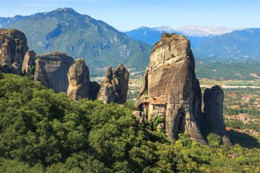 Bu nefes kesici manzara, Meteora 'daki yüksek kaya oluşumları üzerine kurulmuş antik manastırları gösteriyor. Yeşillik ve uzak dağlarla çevrili bu UNESCO Dünya Mirası sitesi, doğal ve mimari güzelliğin çarpıcı bir gösterisini sunuyor..