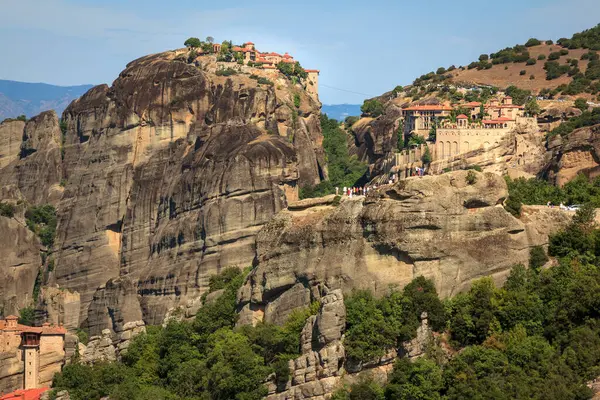 Görüntü, Yunanistan 'daki nefes kesen Meteora Manastırlarının eşsiz bir şekilde yüksek kayalık sütunlar üzerinde yer aldığını gösteriyor. Bu mimari harikalar, doğa ve maneviyatın bir karışımını temsil eden yemyeşil ve dramatik manzaralarla çevrilidir..