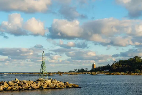 Kayalık sahilde yeşil bir deniz feneri bulunan manzaralı bir manzara. Su yukarıdaki bulutları yansıtır ve sakin bir atmosfer yaratır. Işık, Danimarka 'nın Svaneke, Bornholm kıyı şeridi boyunca bulunan gemiler için güvenli bir giriş sinyali veriyor.