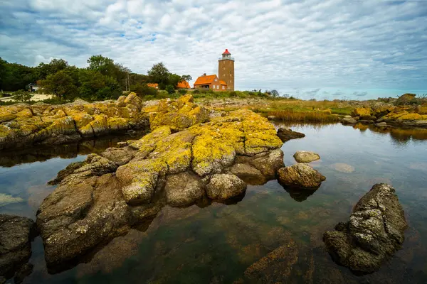 Huzurlu bir su kütlesi ile çevrili kayalık bir kıyı şeridinin üzerinde pitoresk bir deniz feneri duruyor. Gökyüzü dramatik bulutlarla doludur ve kıyı manzarasının güzelliğini artırır. Svaneke, Bornholm, Danimarka.