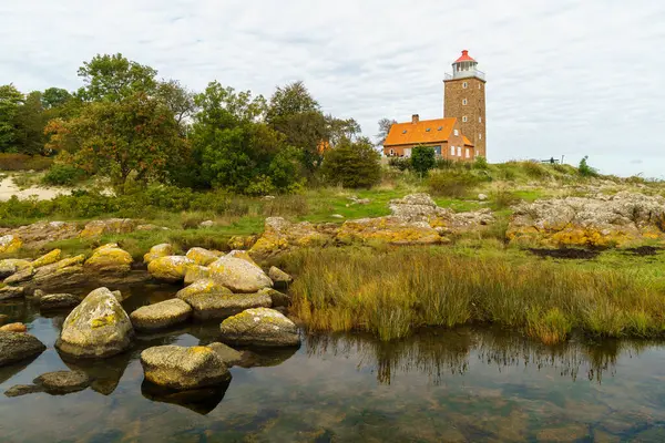 Canlı yeşillik ve sakin sularla çevrili kayalık bir sahil şeridinde deniz feneri bulunan pitoresk bir sahnedir. Kule kırmızı bir çatı ile kaplanmış, ilginç ve davetkar bir atmosfer yaratıyor. Svaneke, Bornholm, Danimarka.