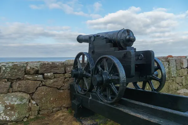 Tahta bir platforma yerleştirilmiş eski bir top, hareket için tekerlekleri olan, taş bir duvara ve okyanus zeminine dayalı. Gökyüzü parçalı bulutlu ve tarihsel atmosfere ekleniyor. Hıristiyanlar, Bornholm, Danimarka.