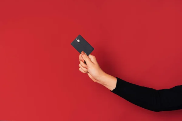 Mão Das Mulheres Segurando Cartão Crédito Preto Contra Fundo Vermelho — Fotografia de Stock