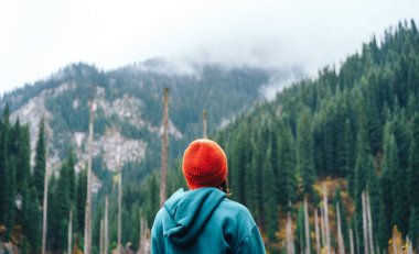 Dağların önünde yeşil köknar ile duran bir kadın.
