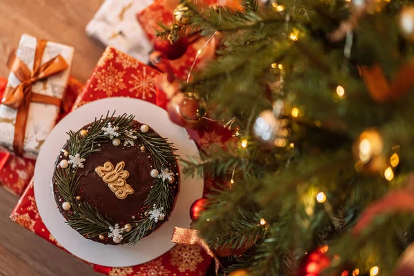 Chocolate covered Christmas cake with Christmas tree branches and numbers 2023 under the tree.