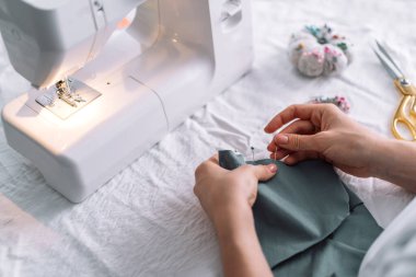 Bayan dikiş makinesinin önündeki kumaşı iğnelerle onarıyor..