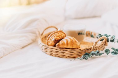 Wicker tray with croissants on white bed linen.