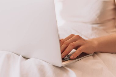 Lady working on a laptop in bed with white linens.