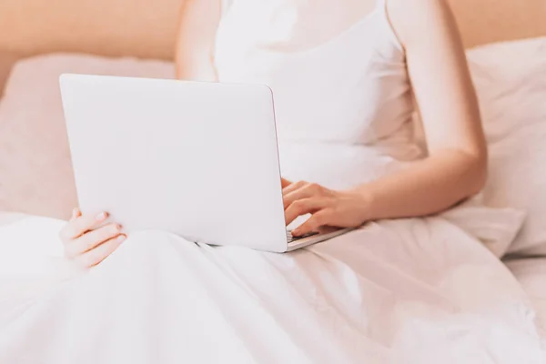Lady working on a laptop in bed with white linens.