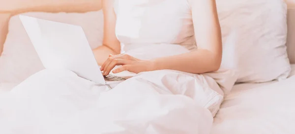 Lady working on a laptop in bed with white linens.