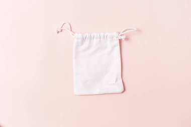 White pouch with a drawstring on a pink background.