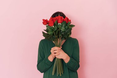Lady with bouquet of red roses against pink background.