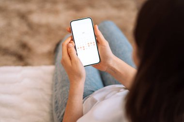 Lady looks in the smartphone days of the calendar menstrual cycle.