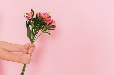 Childrens hands holding bouquet of flowers against pink background. mothers day