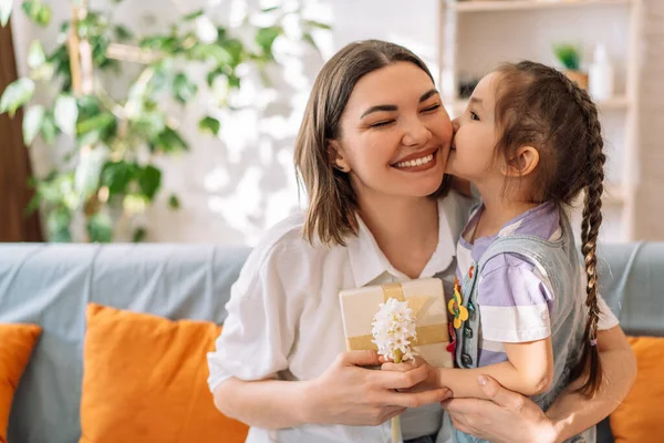Daughter kissed her mother and gave gift with flowers while sitting on the sofa. mothers day