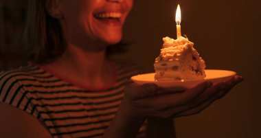 Girl in a dark room blows out candles on a piece of cake.