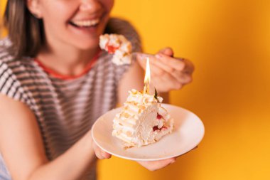 Lady in front of a yellow background eats a meringue roll.