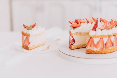 Sliced piece next to mousse cake with strawberries on white table.