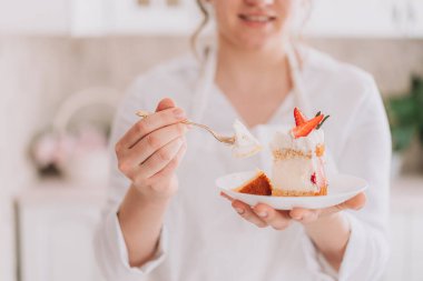 Confectioner in white uniform holding a cut piece of cake with a fork.