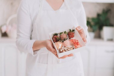 Confectioner in white uniform holding chocolate covered strawberries in gift box.