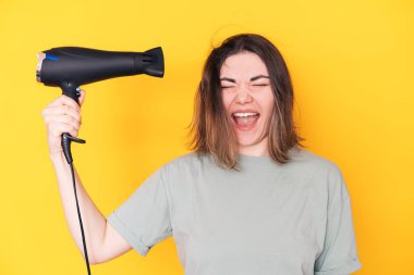Lady drying her hair with hair dryer against yellow background.