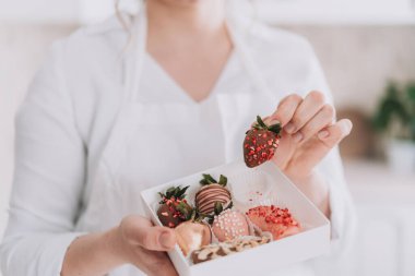 Confectioner in white uniform holding chocolate covered strawberries in gift box.