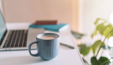 Laptop with coffee cup on desktop with notepad.