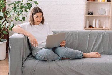 Lady sitting on gray sofa watching movie with laptop.