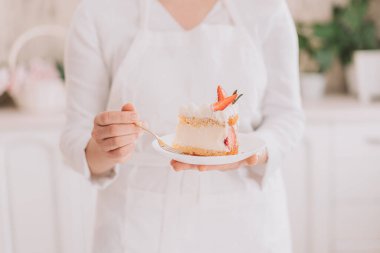 Confectioner in white uniform holding cut piece of mousse cake with strawberries.