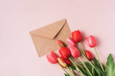 Red blooming tulips with craft envelope on pink background.