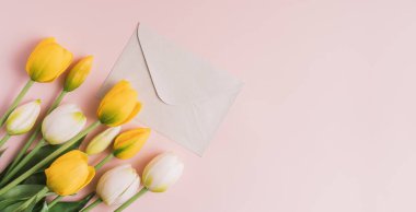 Yellow and white blooming tulips with white envelope on pink background.