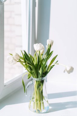 Pencere kenarındaki cam sürahide beyaz laleler..