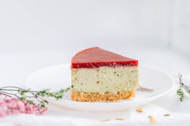 Tabakta fıstıklı cheesecake, beyaz arka planda kurumuş çiçeklere karşı.