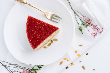 Çam fıstıklı cheesecake tabakta çatalla beyaz arka planda kurumuş çiçeklere karşı.