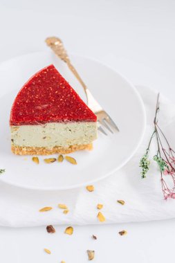 Çam fıstıklı cheesecake tabakta çatalla beyaz arka planda kurumuş çiçeklere karşı.