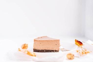 Tabakta çikolatalı cheesecake, çatalla beyaz arka plan ve kurumuş çiçekler..