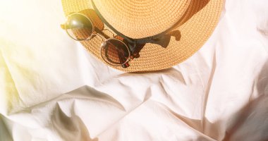 Güneş gözlüğü ve şapka güneş ışınlarının altında beyaz kumaş üzerinde.