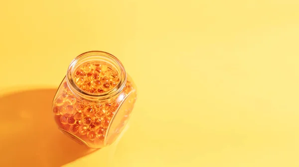 Fish oil capsules in glass jar on yellow background.