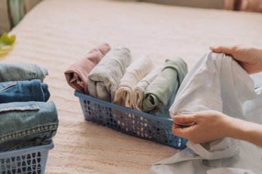 Bayan yatakta otururken elbiselerini kabın içine katlıyor..