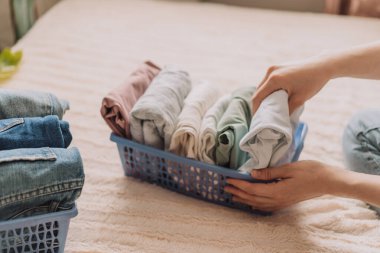 Bayan yatakta otururken elbiselerini kabın içine katlıyor..