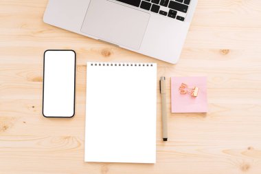 Beyaz ekranlı akıllı telefon, mesaj ya da dizüstü bilgisayarlı ahşap masa reklamları için. Kalem ve pembe çıkartmalı boş not defteri.